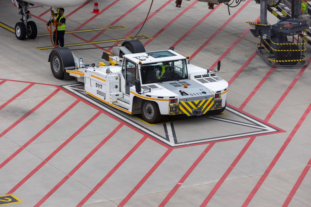 Aircraft tug maneuvering on a runway, preparing for plane departure at a busy airport.